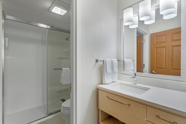 Un baño moderno con cabina de ducha de vidrio, un lavabo blanco y un mueble de tocador de madera.