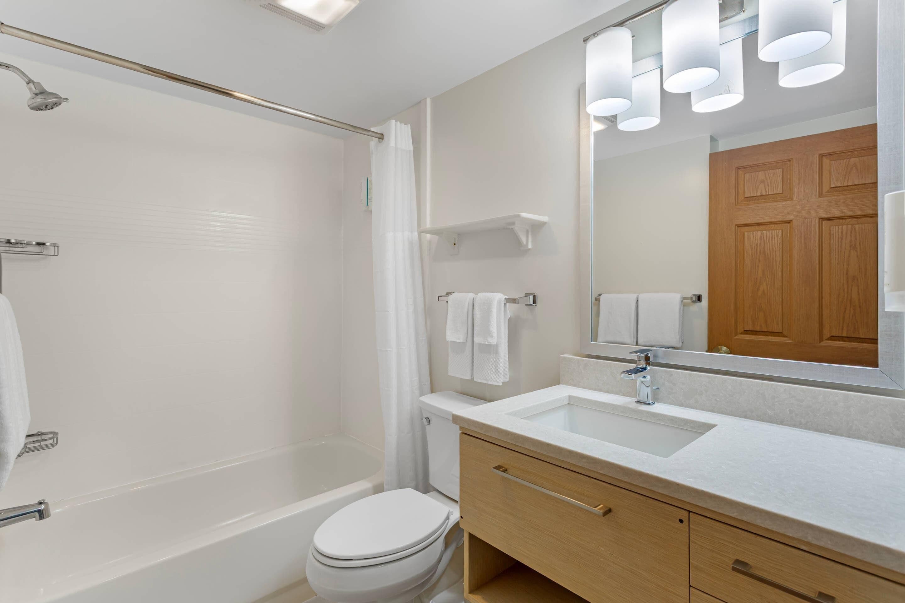 A modern bathroom with a bathtub, toilet, and vanity with a mirror.
