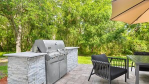 An outdoor kitchen with a built-in grill, a stone accent wall, and a wicker chair. - MainStay Suites Tampa Moffitt-USF (Tampa)