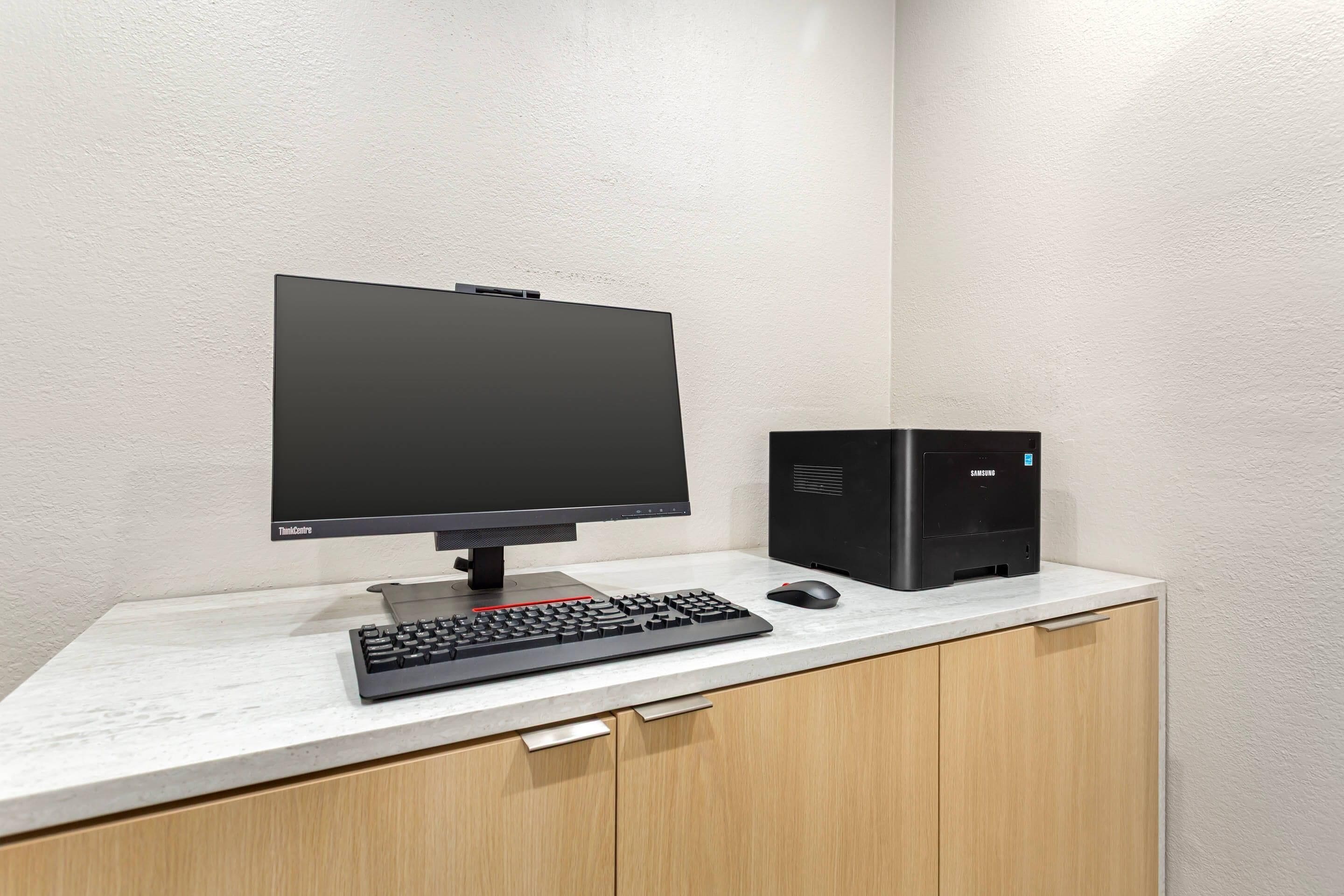 A computer setup with a monitor, keyboard, and tower on a white desk against a plain wall.