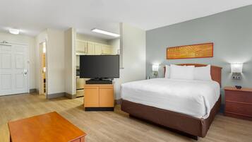Una habitación de hotel con cama, lámparas de noche, televisor, mesa de madera y kitchenette.