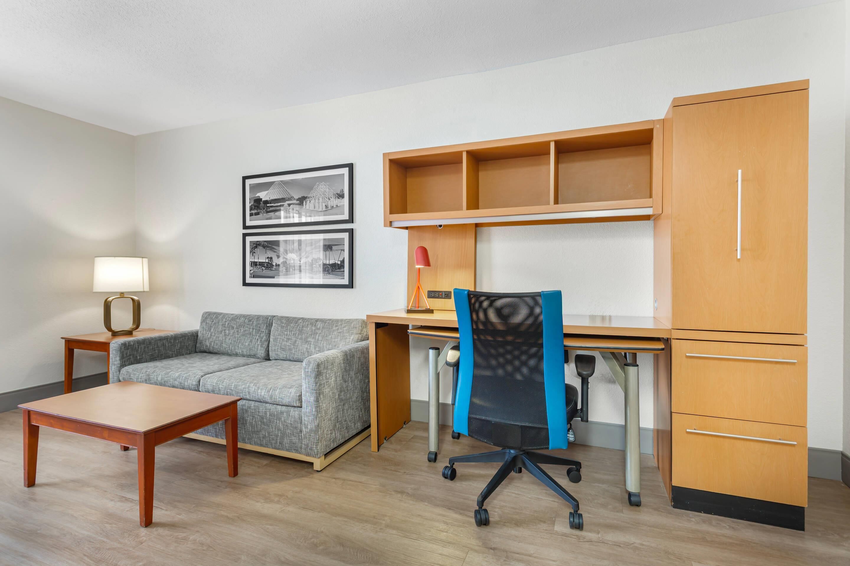 A room with a wooden desk, a cushioned sofa, a small table, and a chair with wheels.