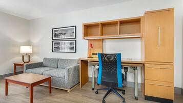 A room with a wooden desk, a cushioned sofa, a small table, and a chair with wheels.