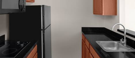 Una cocina compacta con un refrigerador negro, un microondas, un lavamanos y armarios de madera.