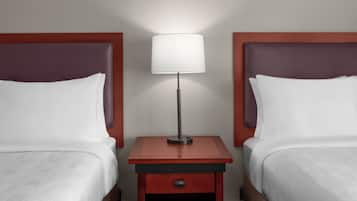 Two beds with white linens, a nightstand with a lamp, and a red wall.