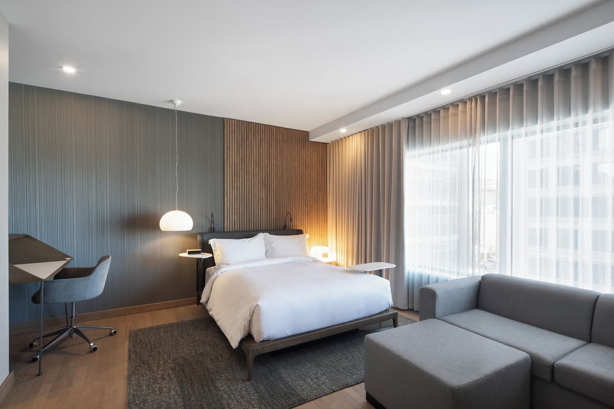 A modern hotel room with a large bed, a desk, a chair, and a sofa.