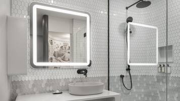 A modern bathroom with a glass shower enclosure, a large mirror with LED lighting, and a white vanity with a sink and towel storage.