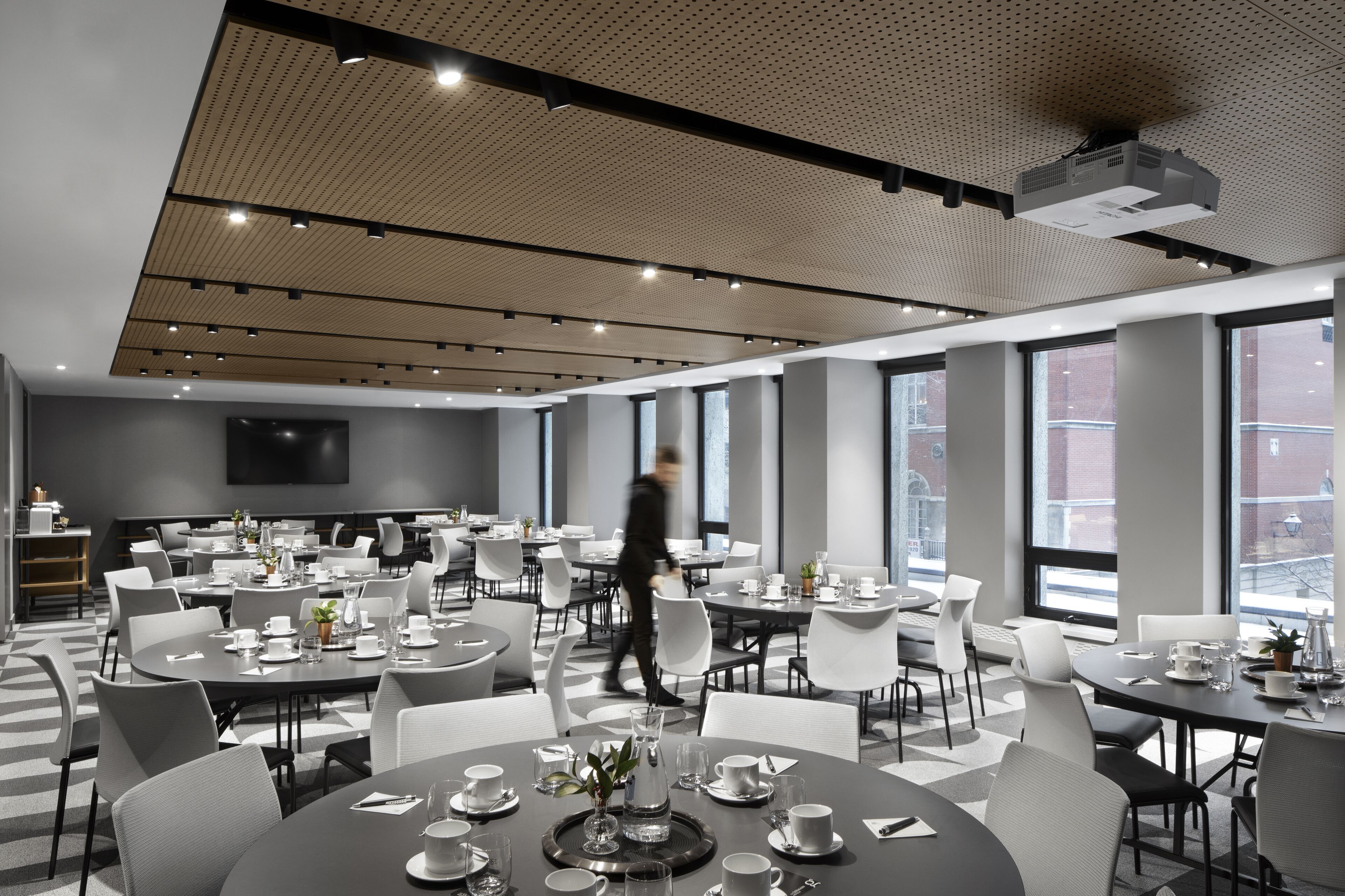 A modern conference room with multiple tables and chairs, large windows, and a ceiling projector.
