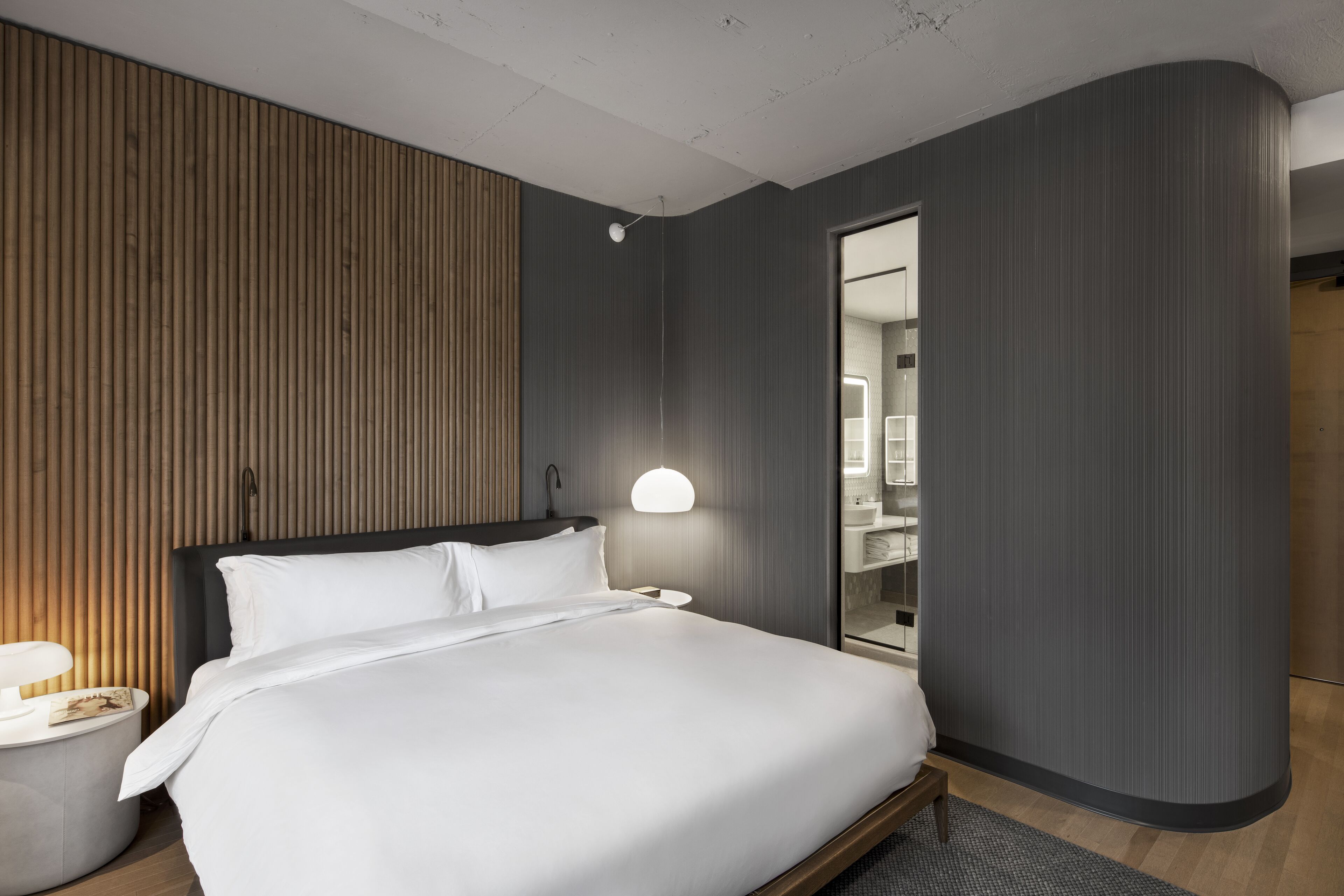 A modern hotel room with a large bed, a bedside table, a lamp, and a mirror.