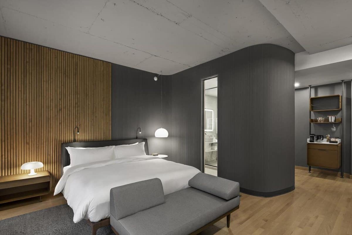 A modern bedroom with a bed, bedside table, lamp, and a bench.