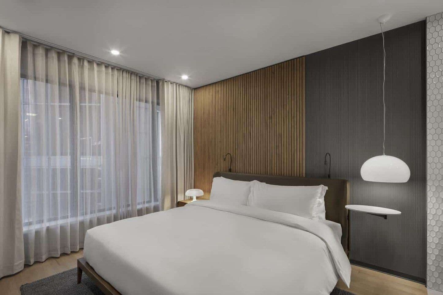 A modern bedroom with a large bed, a wooden accent wall, and a pendant light.