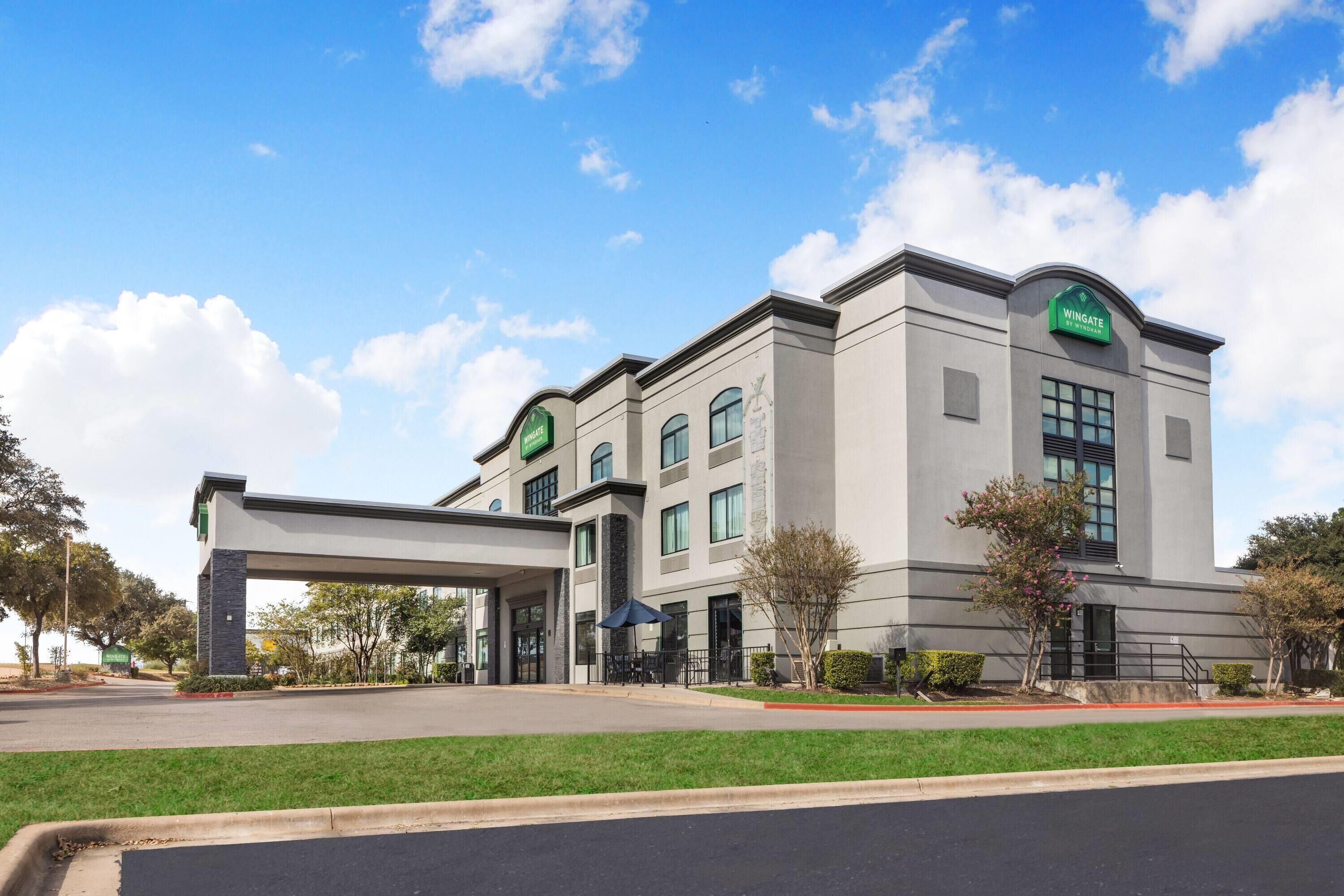 A modern hotel with a large entrance canopy, multiple windows, and a green sign indicating the name.