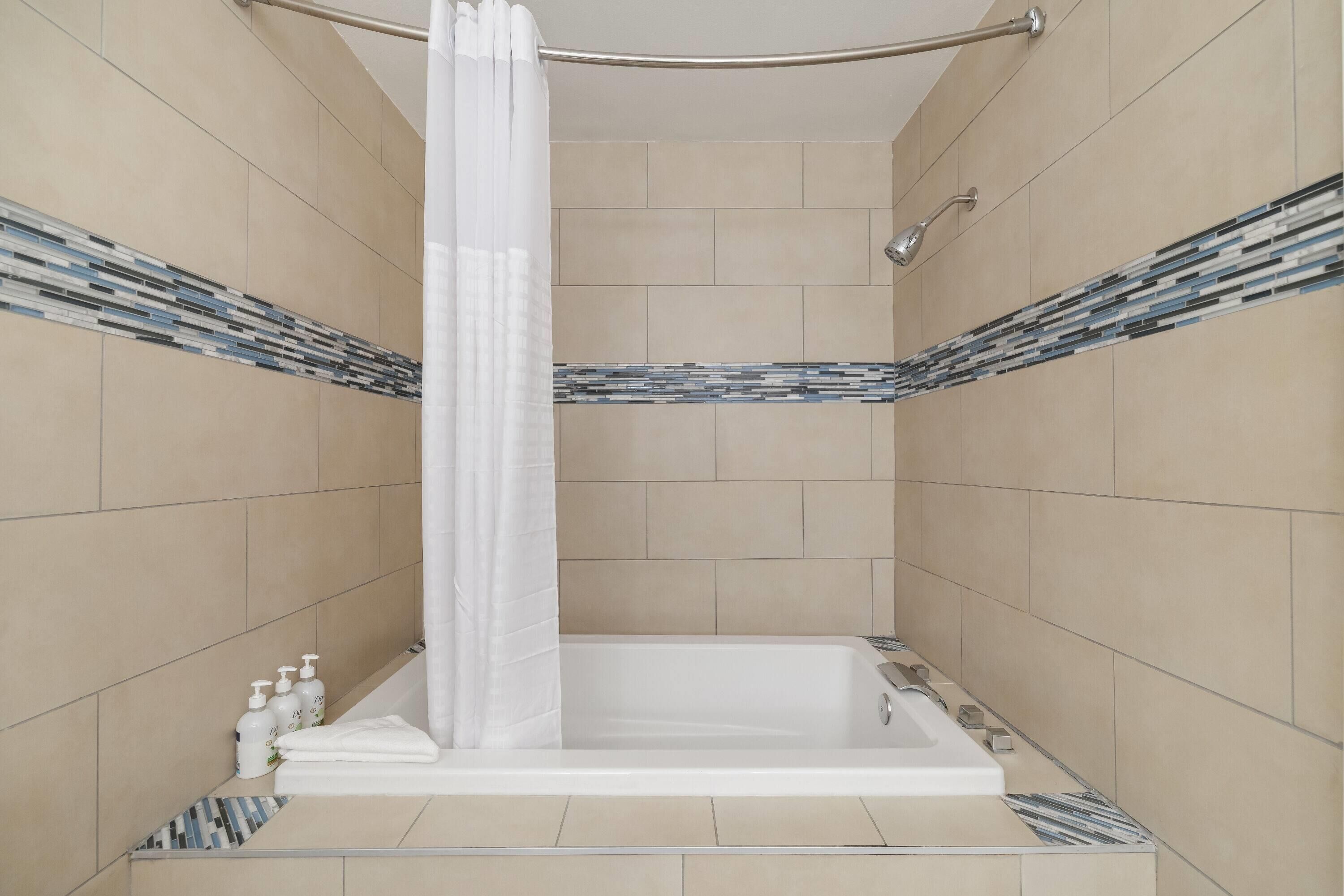 A modern bathroom with a bathtub, shower, and tiled walls.