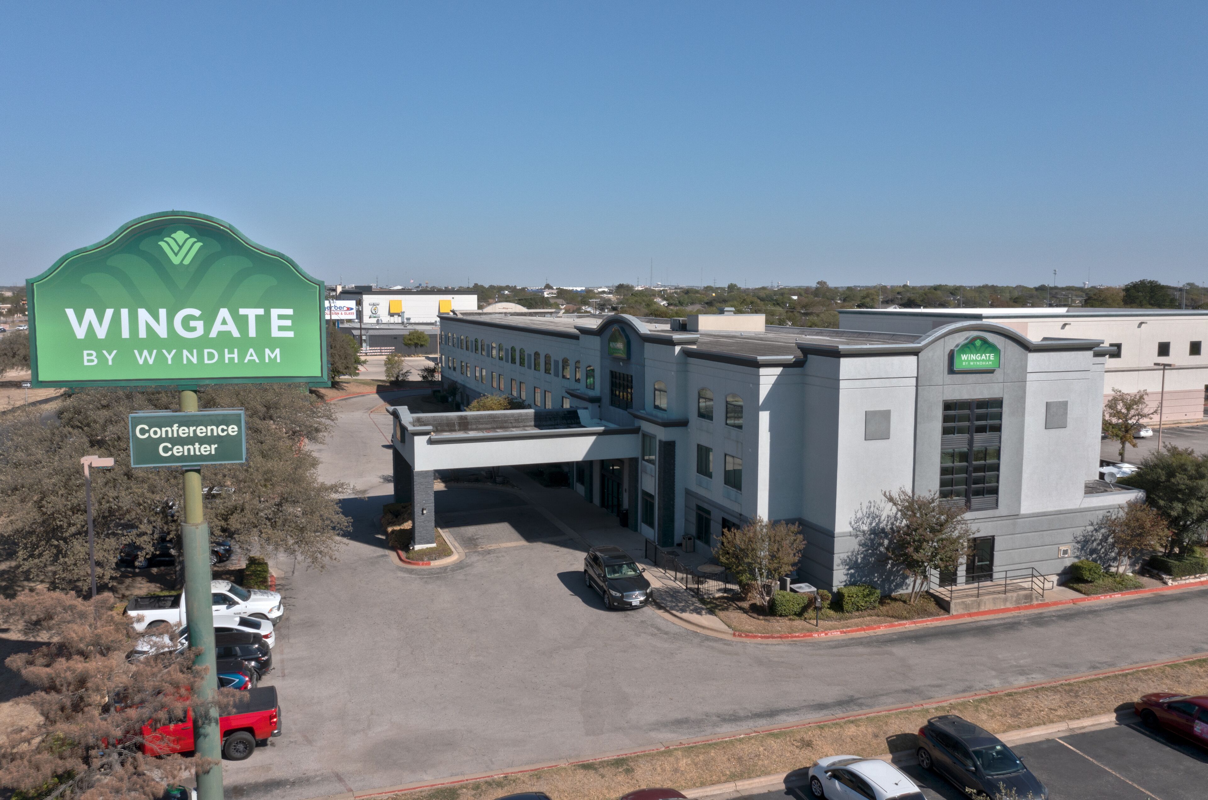 Un edificio con un cartello verde che riporta "Wingate by Wyndham Conference Center" e un parcheggio con diverse auto.
