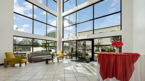 A spacious indoor area with large windows, a yellow armchair, a gray sofa, and a table with a red tablecloth. - Wingate by Wyndham - Round Rock (Round Rock)