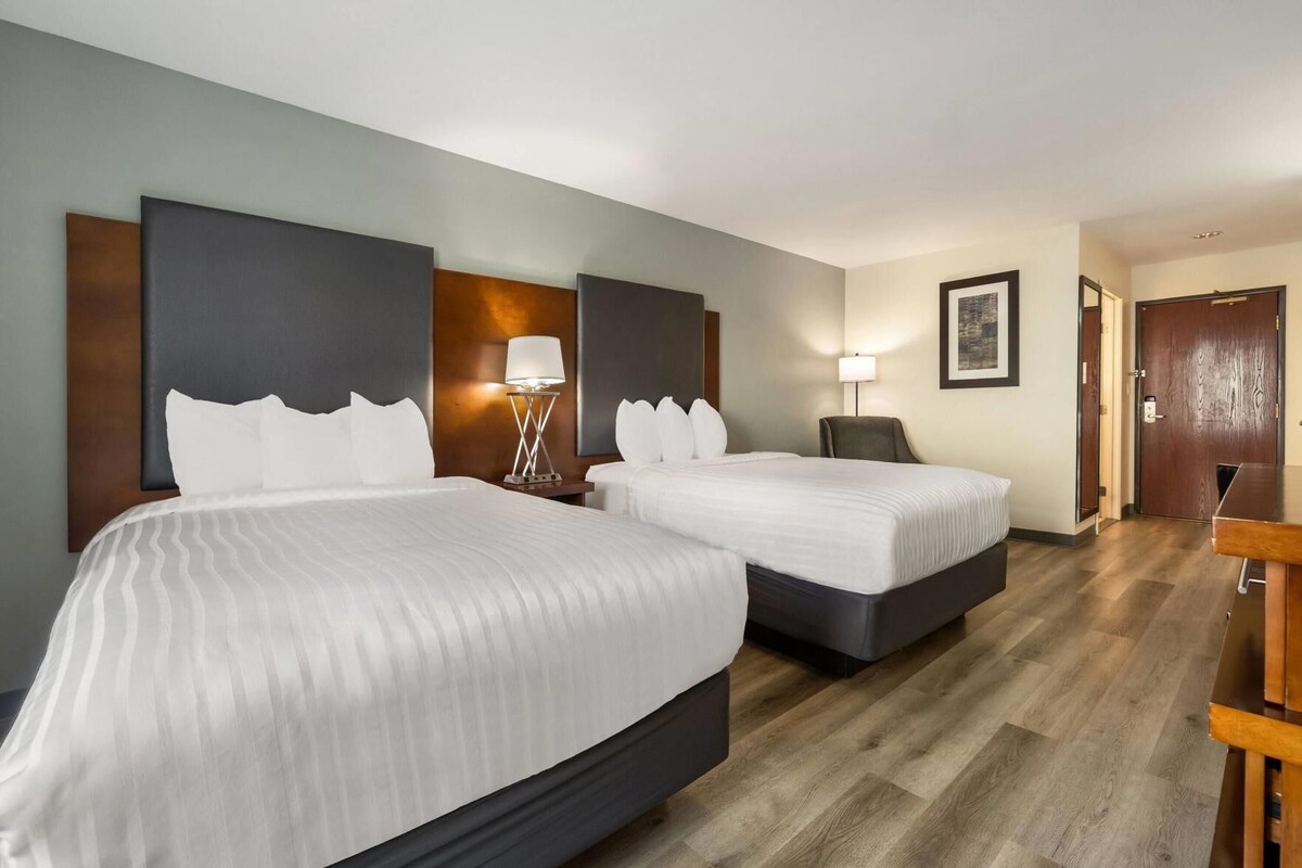 A hotel room with two beds, a desk, a chair, and a door.