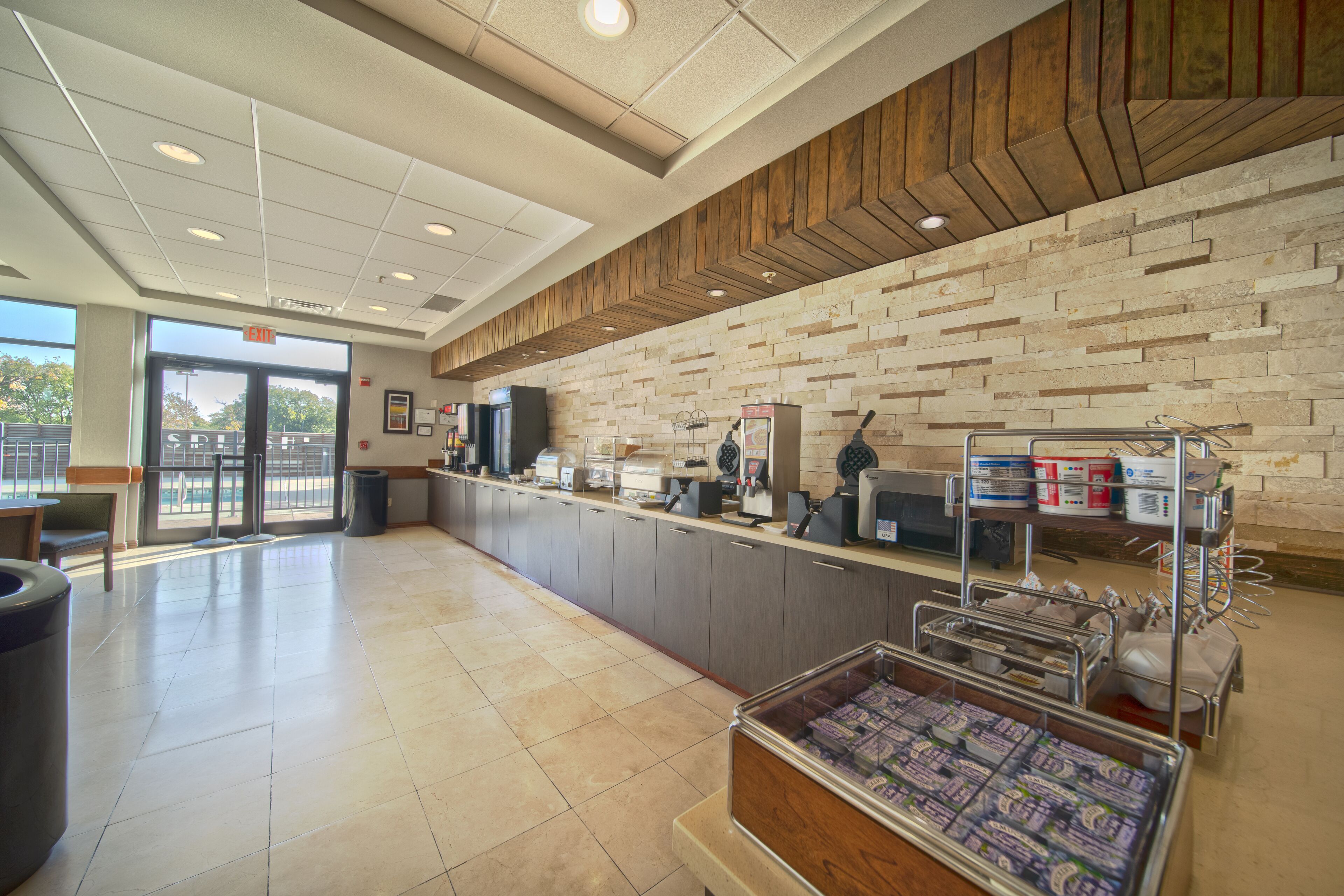 A clean, modern reception area with a wooden accent wall, a counter with various appliances, and a trash bin.