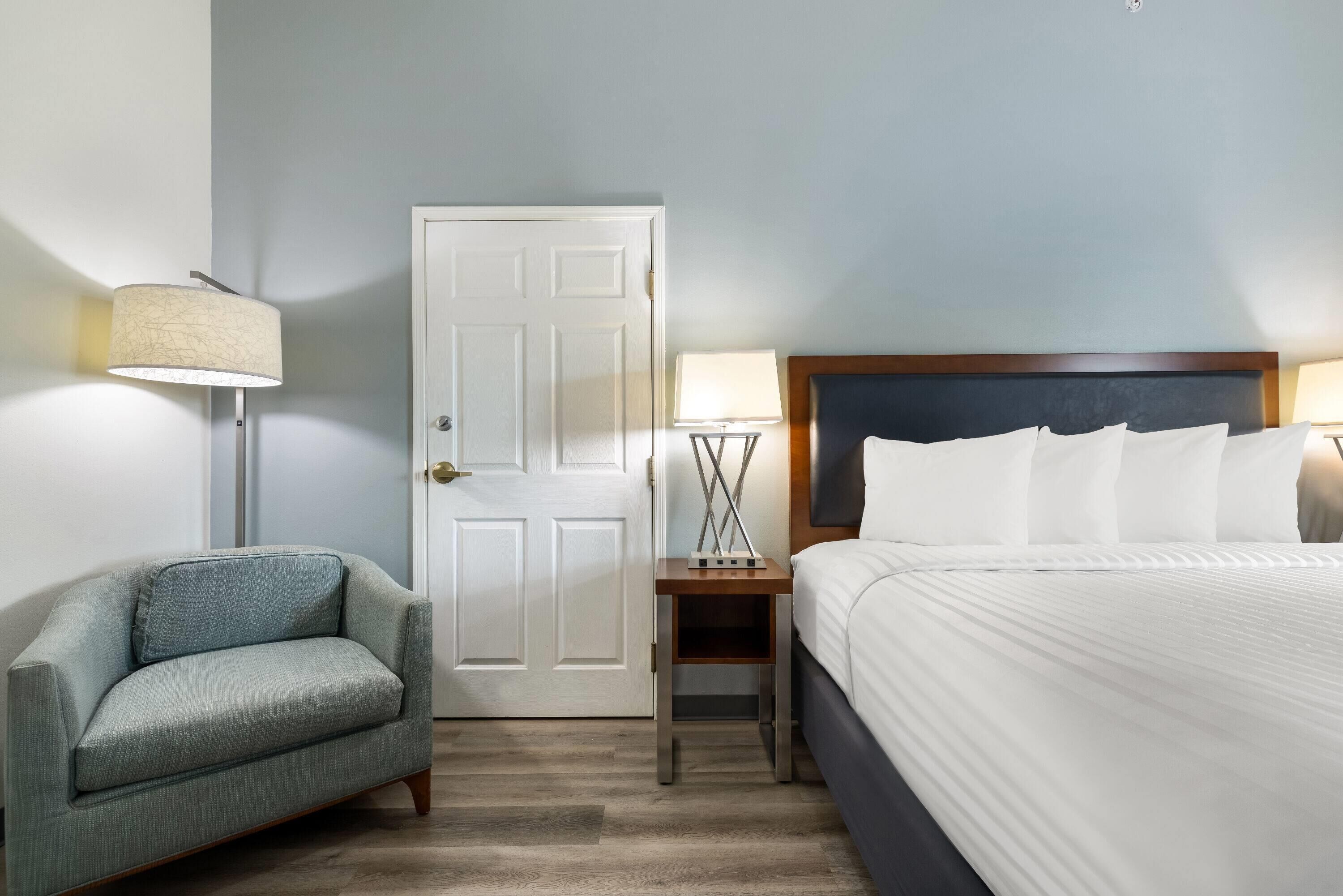 A hotel room with a bed, a nightstand, a lamp, and a chair.