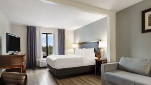 A hotel room with a bed, a desk, a television, a sofa, and a window with curtains. - Wingate by Wyndham - Round Rock (Round Rock)