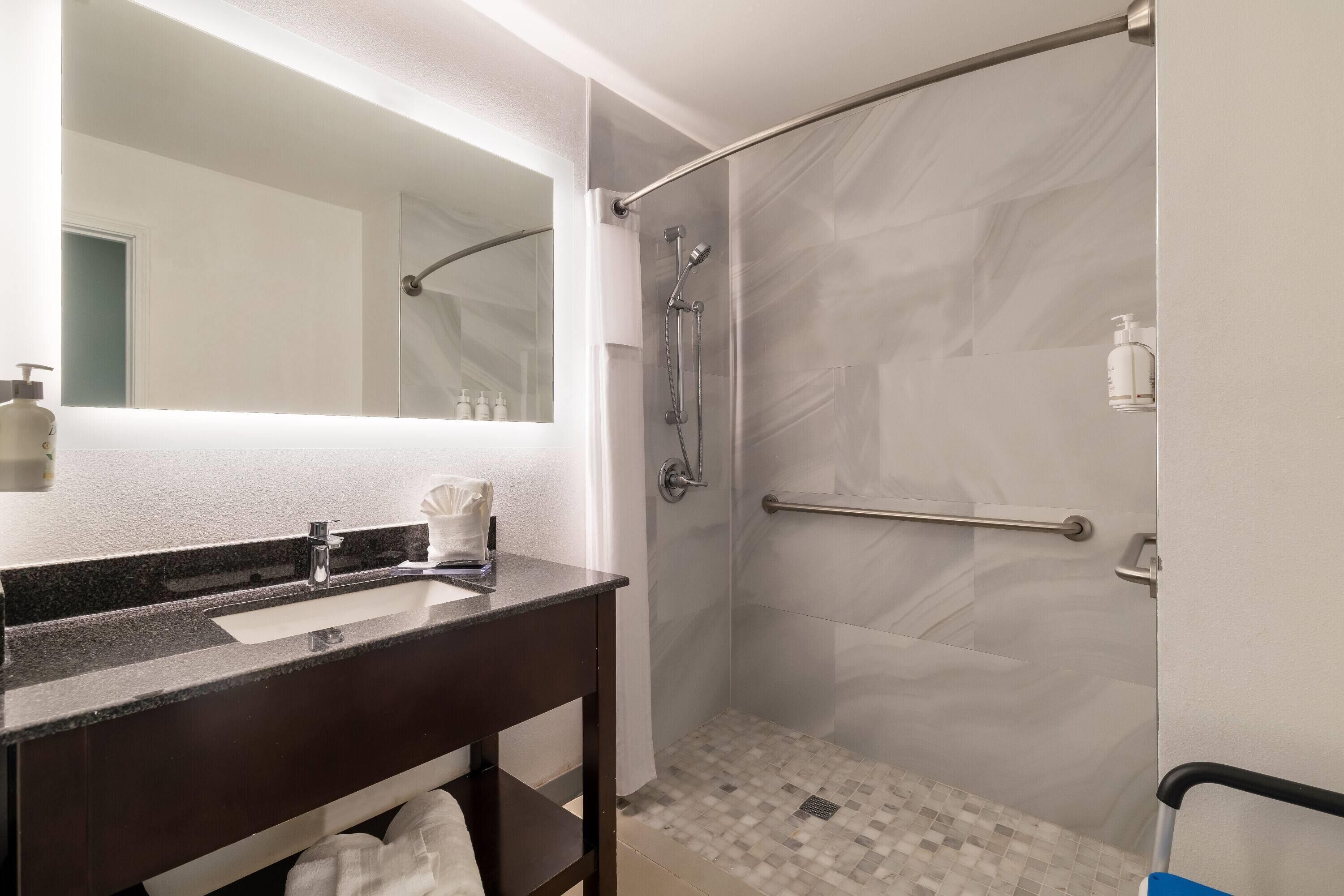 A bathroom with a dark granite sink, a large mirror, a shower with a glass door, and a tiled floor.