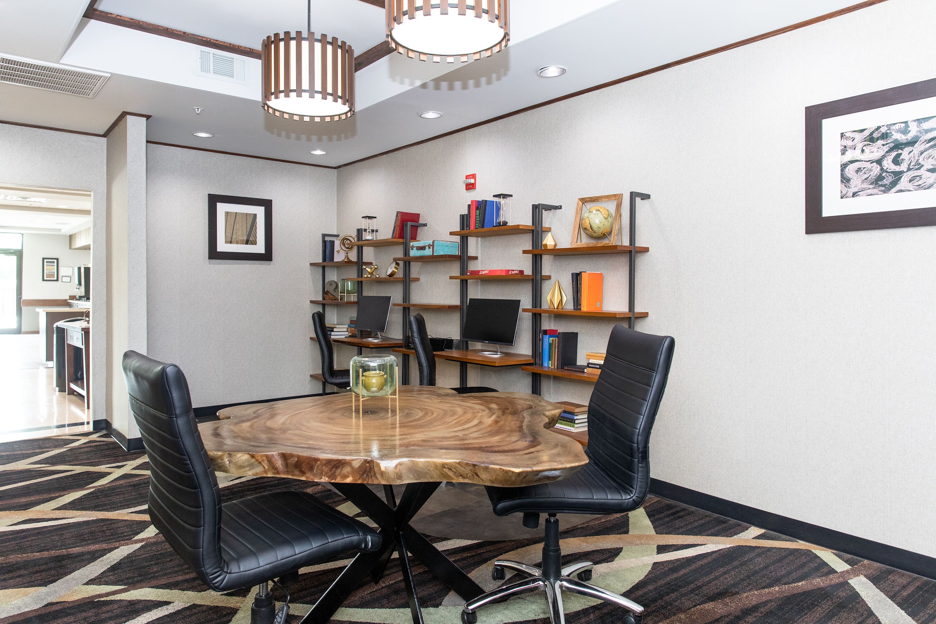 A conference room with a round wooden table, black leather chairs, and a bookshelf with books and decorative items.