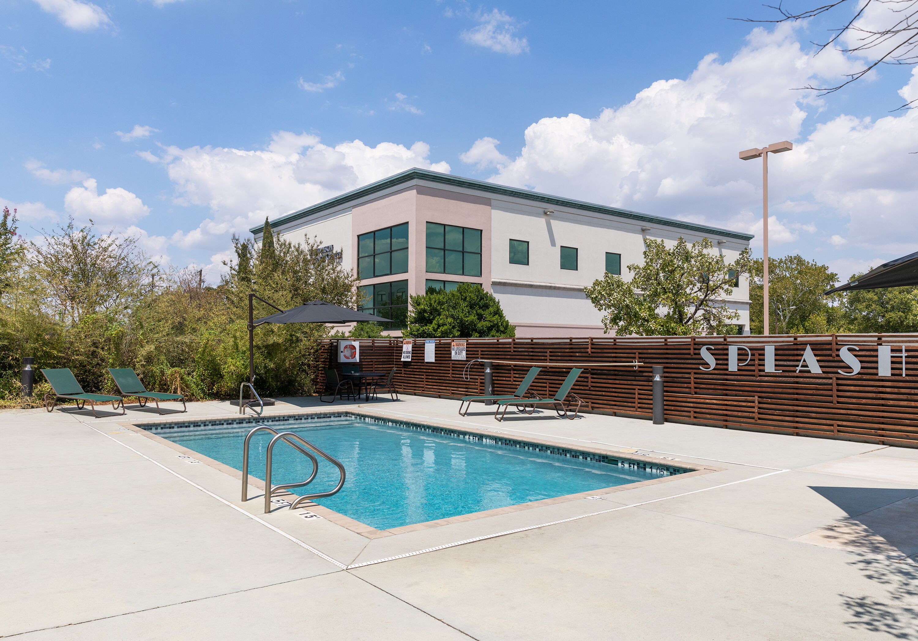 A swimming pool with lounge chairs and a wooden fence labeled "SPLASH".