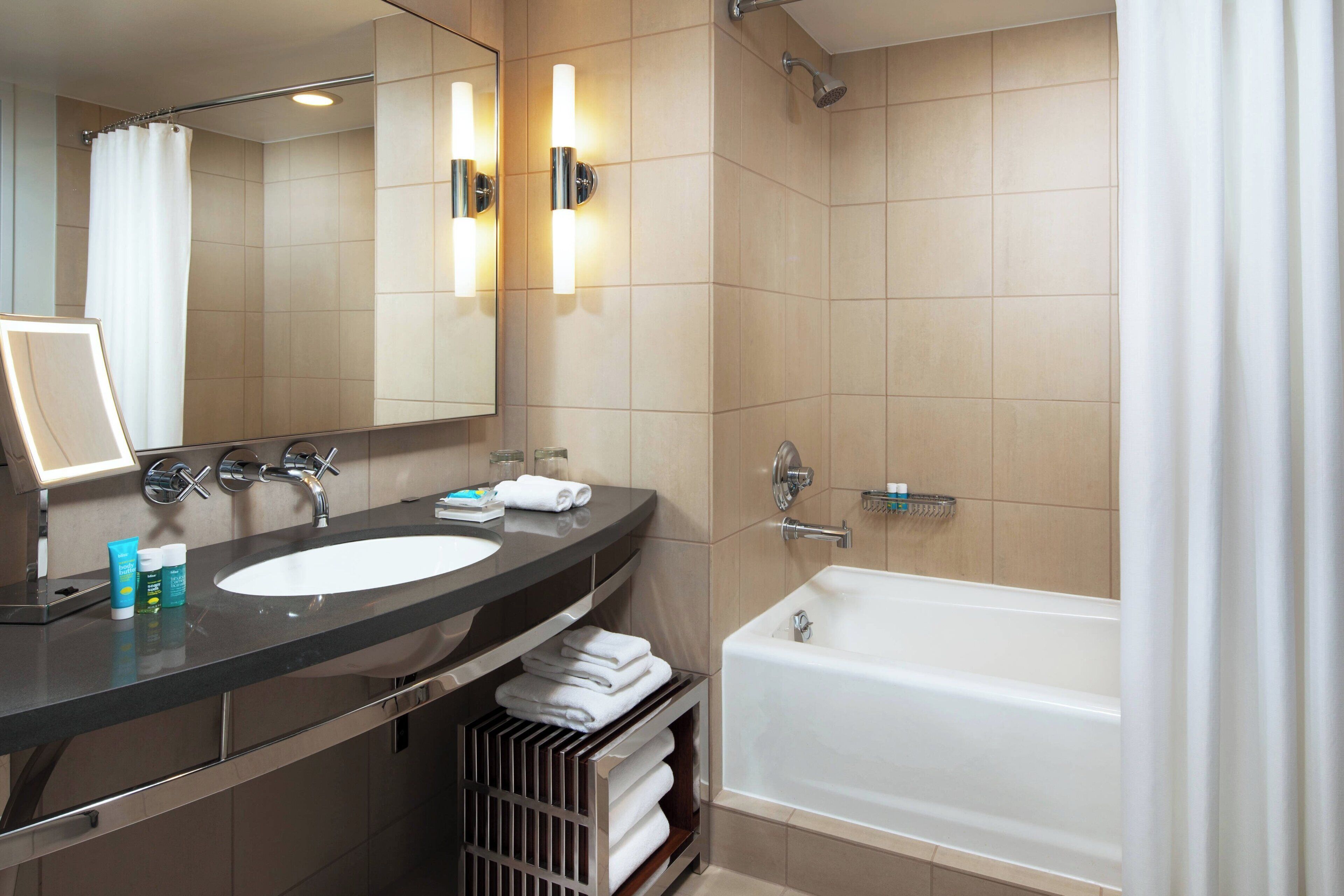 A modern bathroom with a large mirror, two sinks, a bathtub, and a shower.