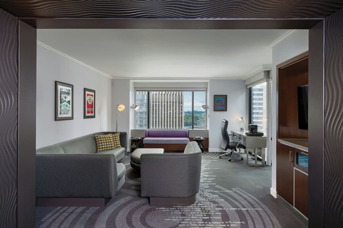 A hotel room with a sofa, armchair, and a desk with a chair.