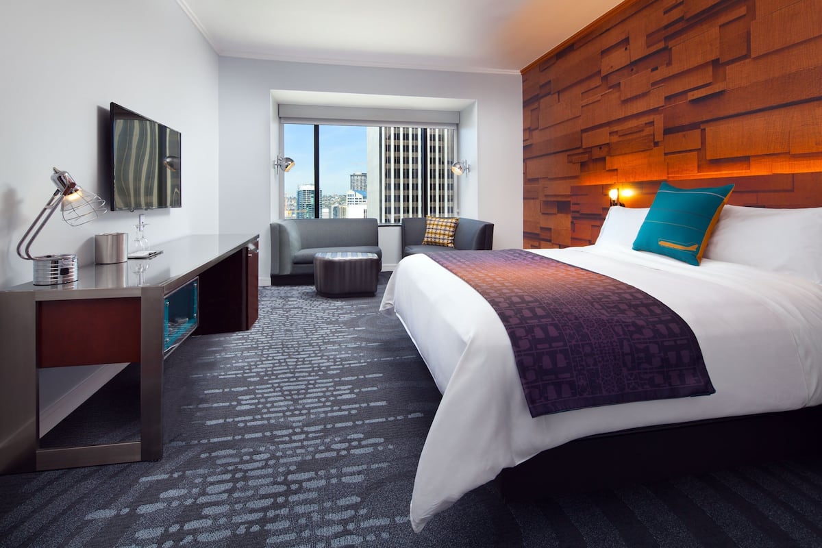 A hotel room with a large bed, a desk, a chair, and a view of the city through the window.