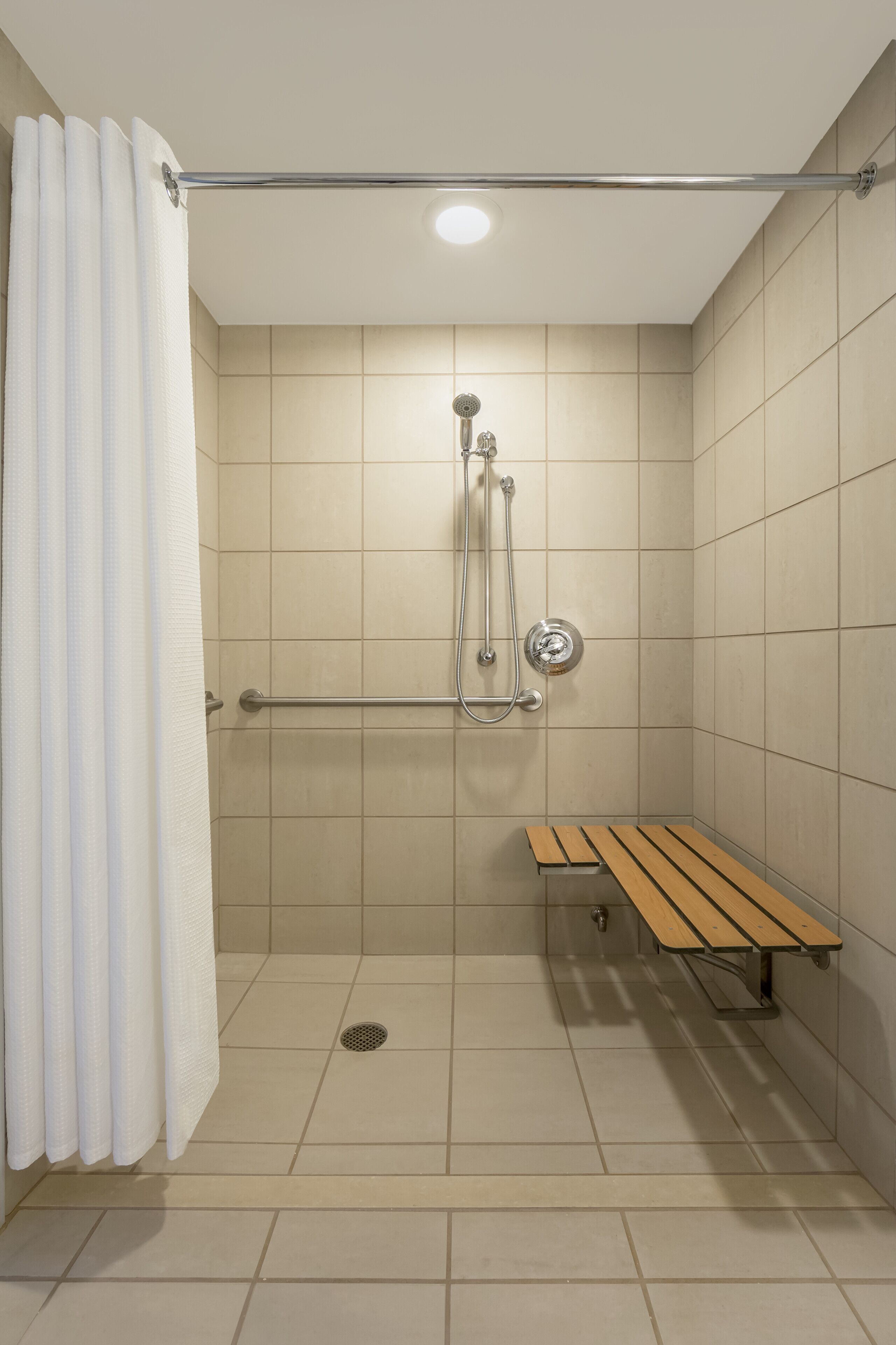 A shower area with a bench, a showerhead, and a handrail.