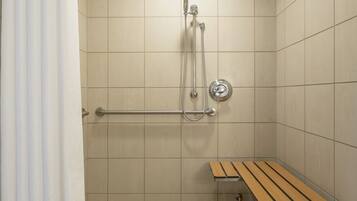 A shower area with a bench, a showerhead, and a handrail.
