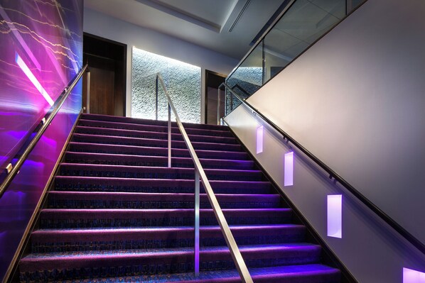 A modern staircase with purple carpet and glass railings, leading to a room with a large window and a textured wall. - W Seattle (Seattle)