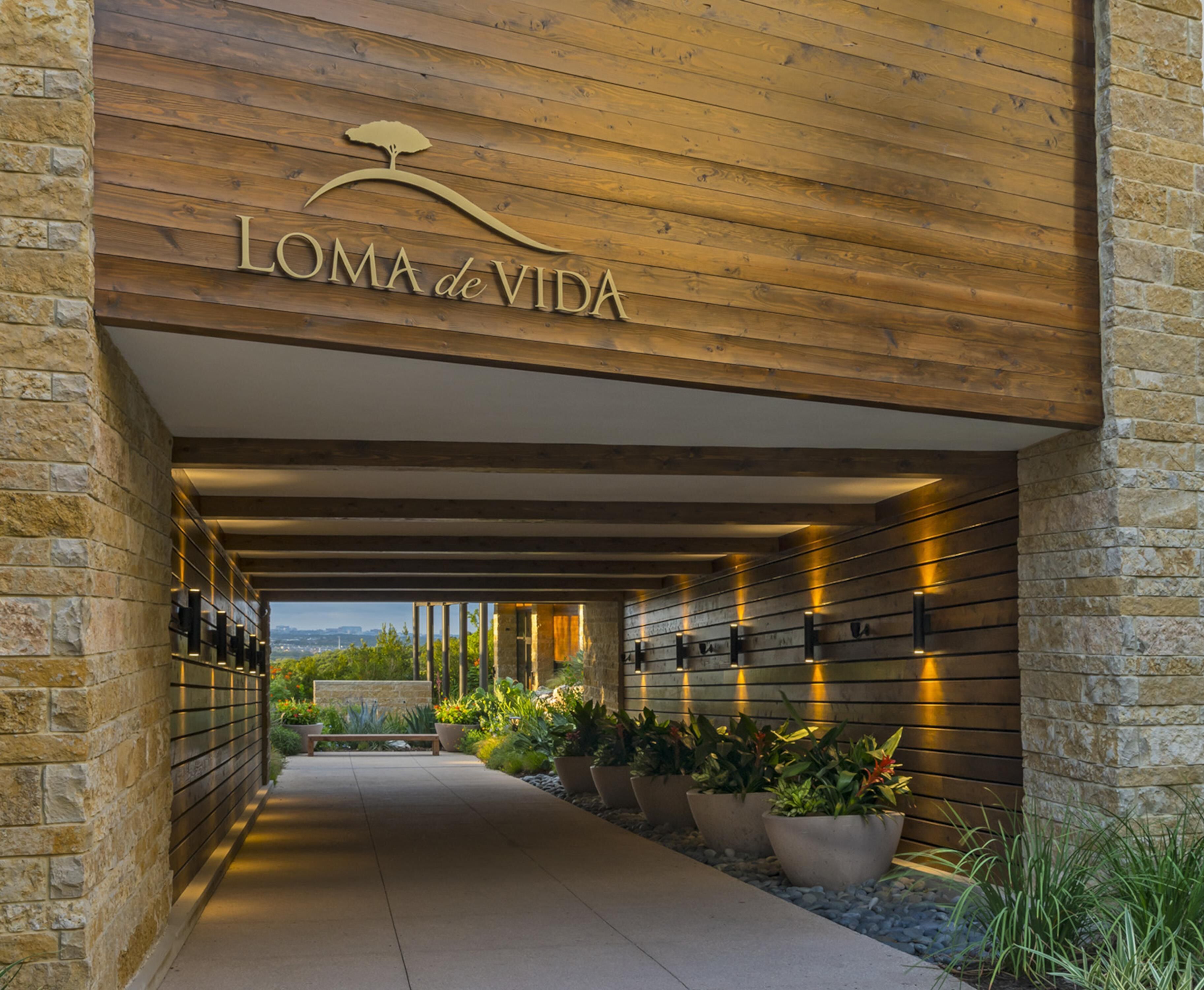 A modern building entrance with a wooden ceiling and stone walls, featuring a sign that reads 'Loma de Vida.'