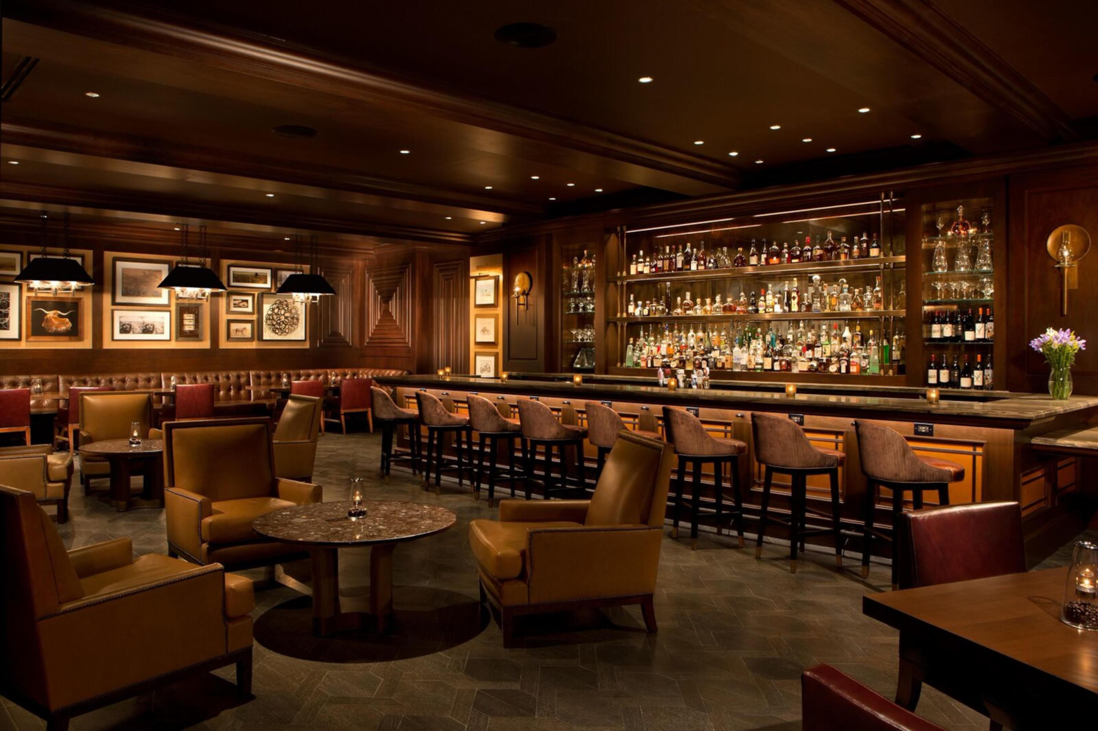 A bar area with multiple seating options, a bar counter, and a variety of bottles and glasses.