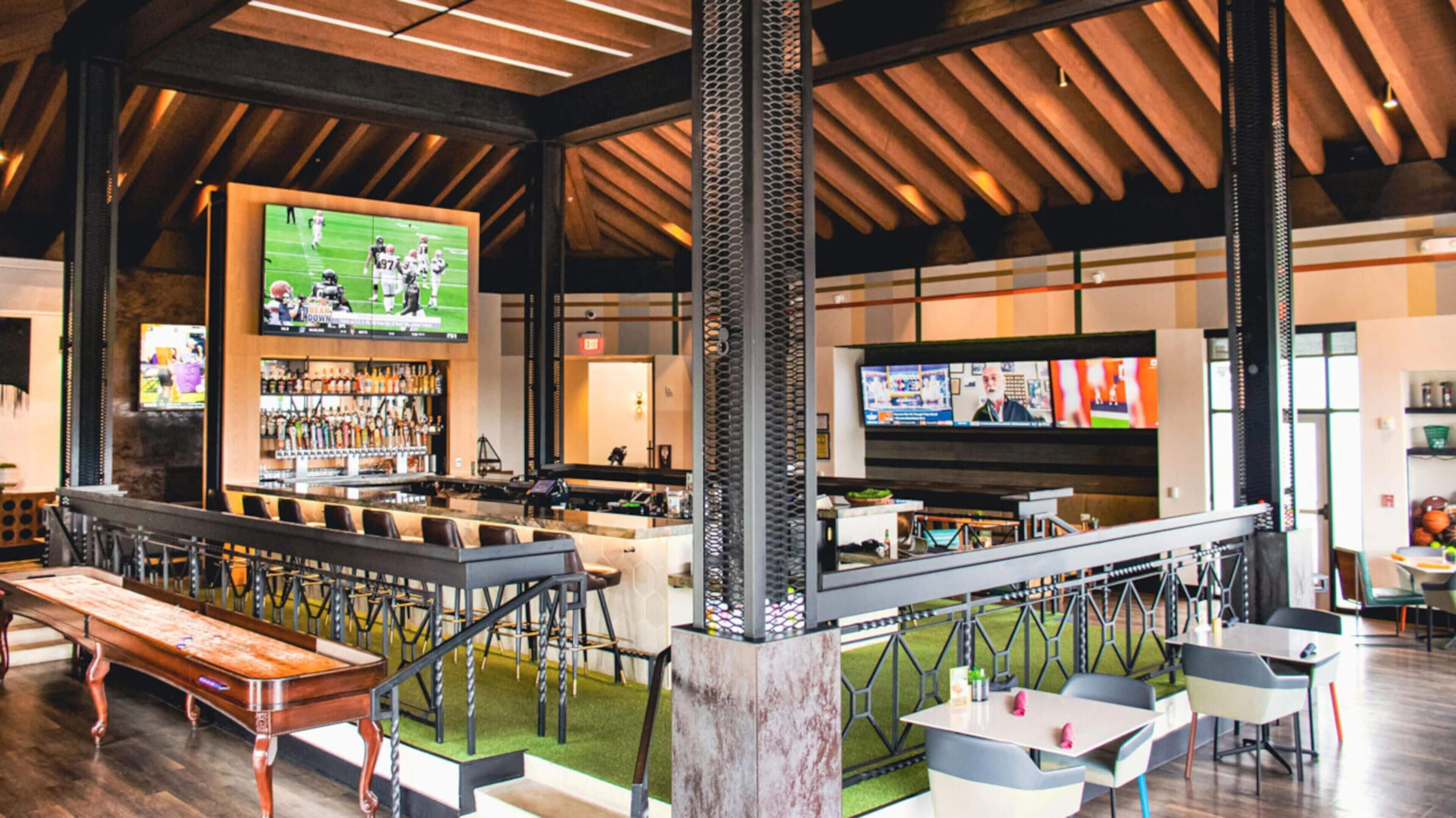 A spacious bar area with multiple seating options, a large screen displaying sports, and a modern interior design.