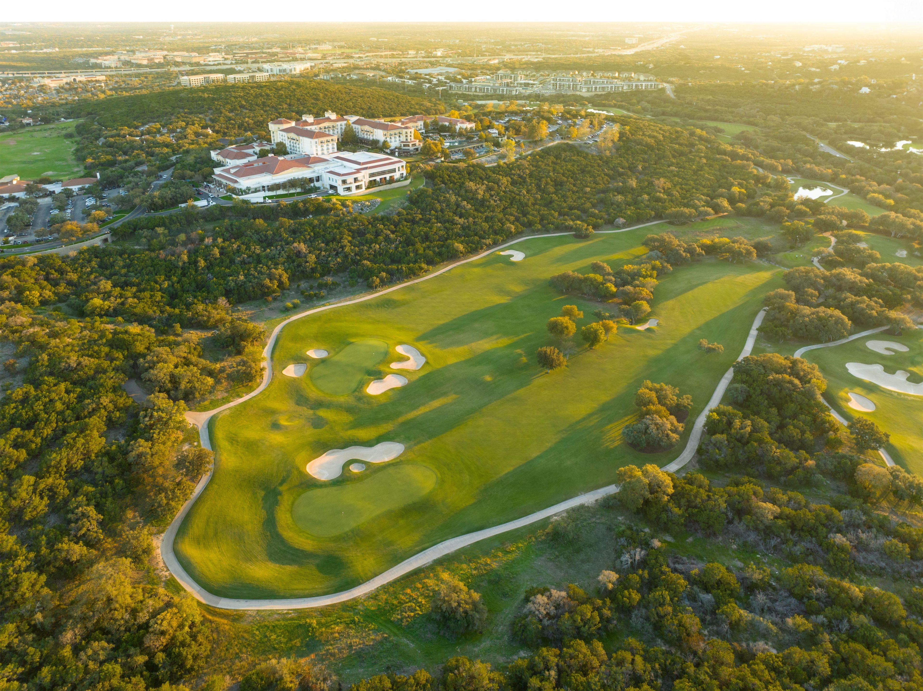 An aerial view of a golf course with a clubhouse and surrounding wooded area.