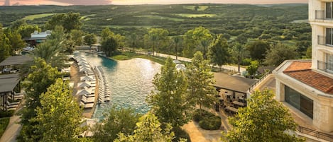 A resort with a swimming pool, lounge chairs, and a view of the surrounding landscape.