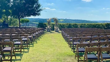 An outdoor seating area with rows of wooden chairs and a grassy path leading to a decorative archway.