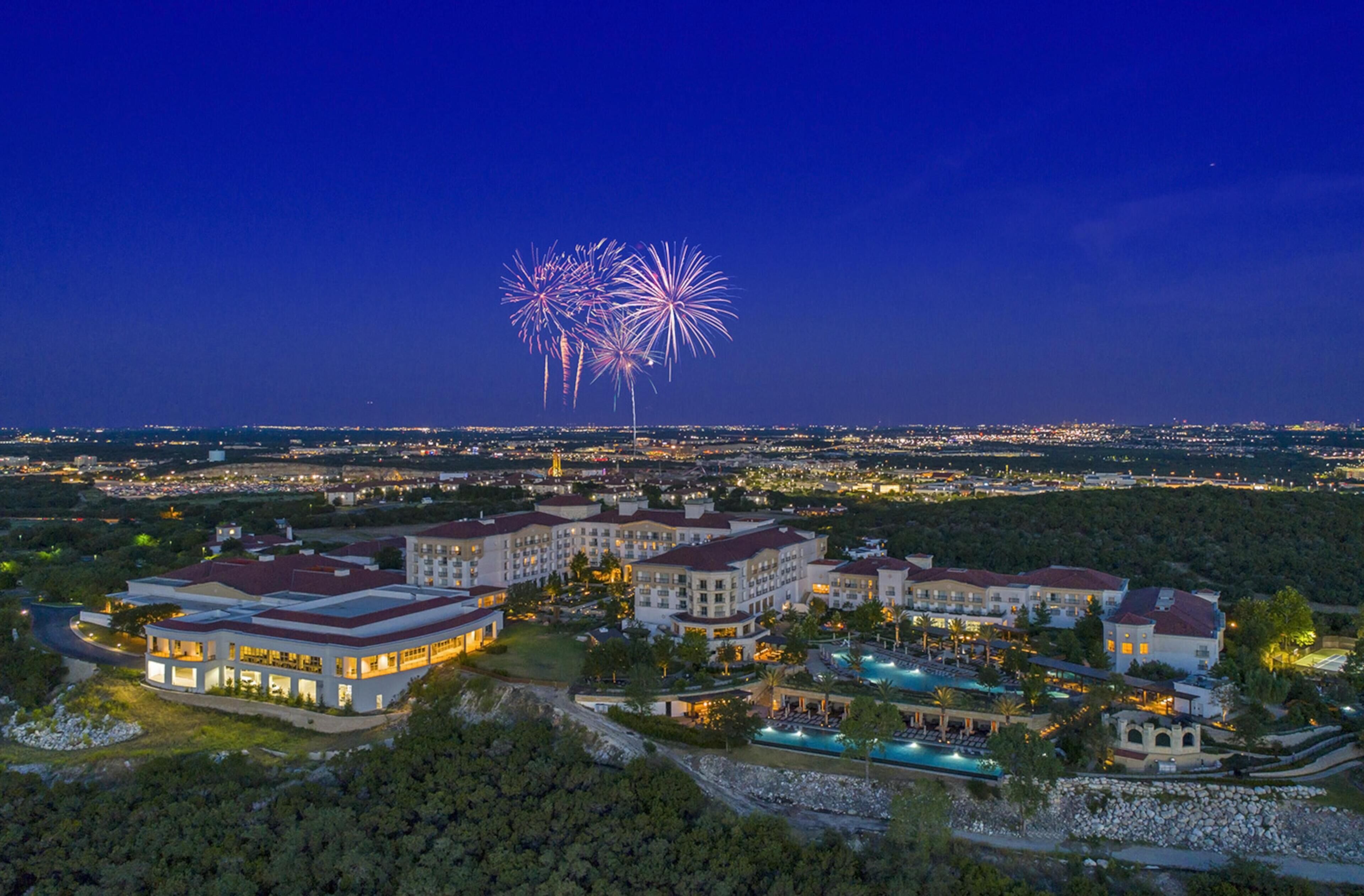 Ein Resort mit mehreren Gebäuden, einem Swimmingpool und Blick auf Feuerwerk in der Ferne.