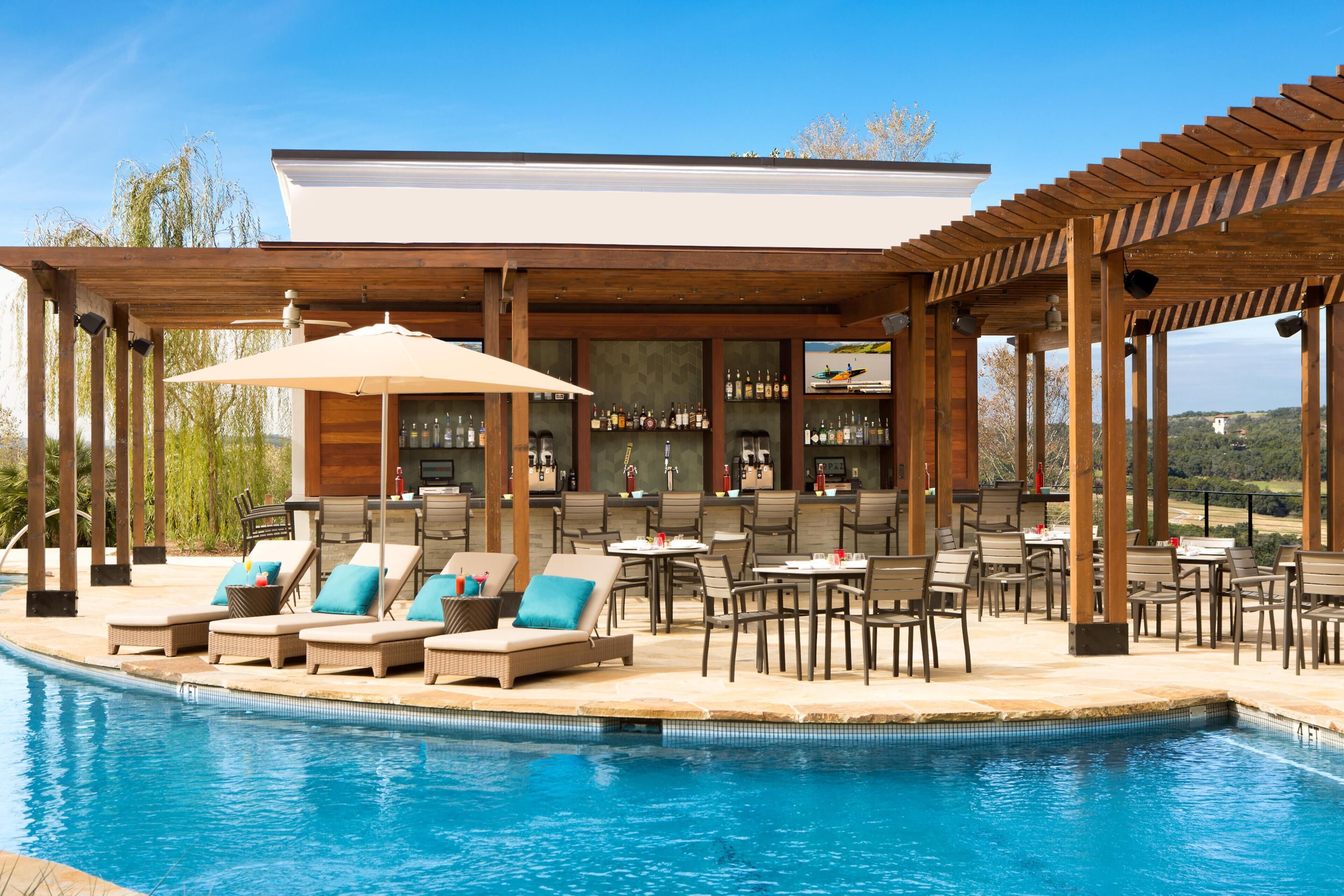 Un área junto a la piscina con sillones reclinables, un bar y una zona de estar techada.