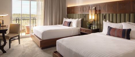 A hotel room with two beds, a desk, a chair, and a balcony with a view.