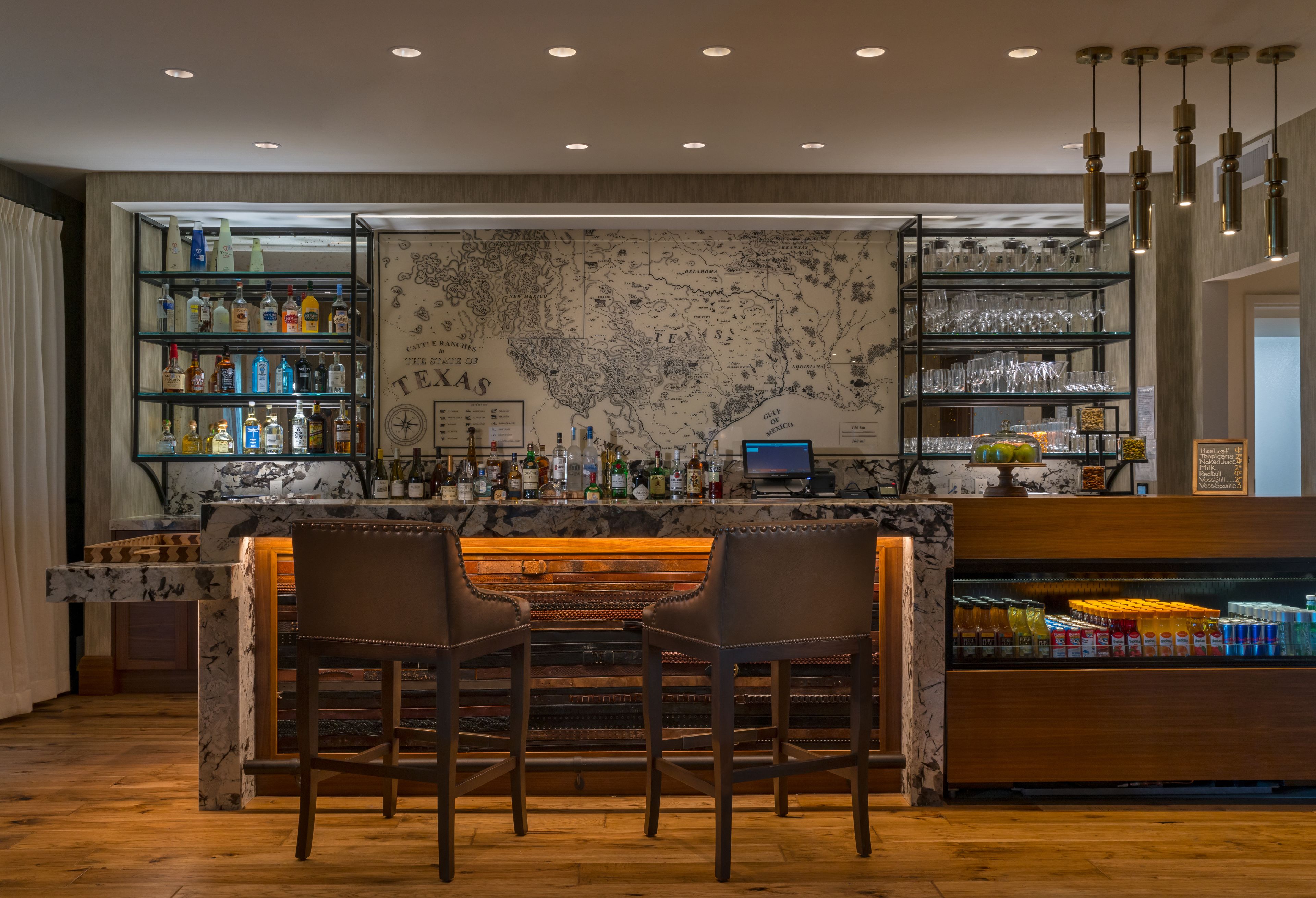 A bar area with a marble countertop, two leather chairs, shelves with bottles and glasses, and a map on the wall.