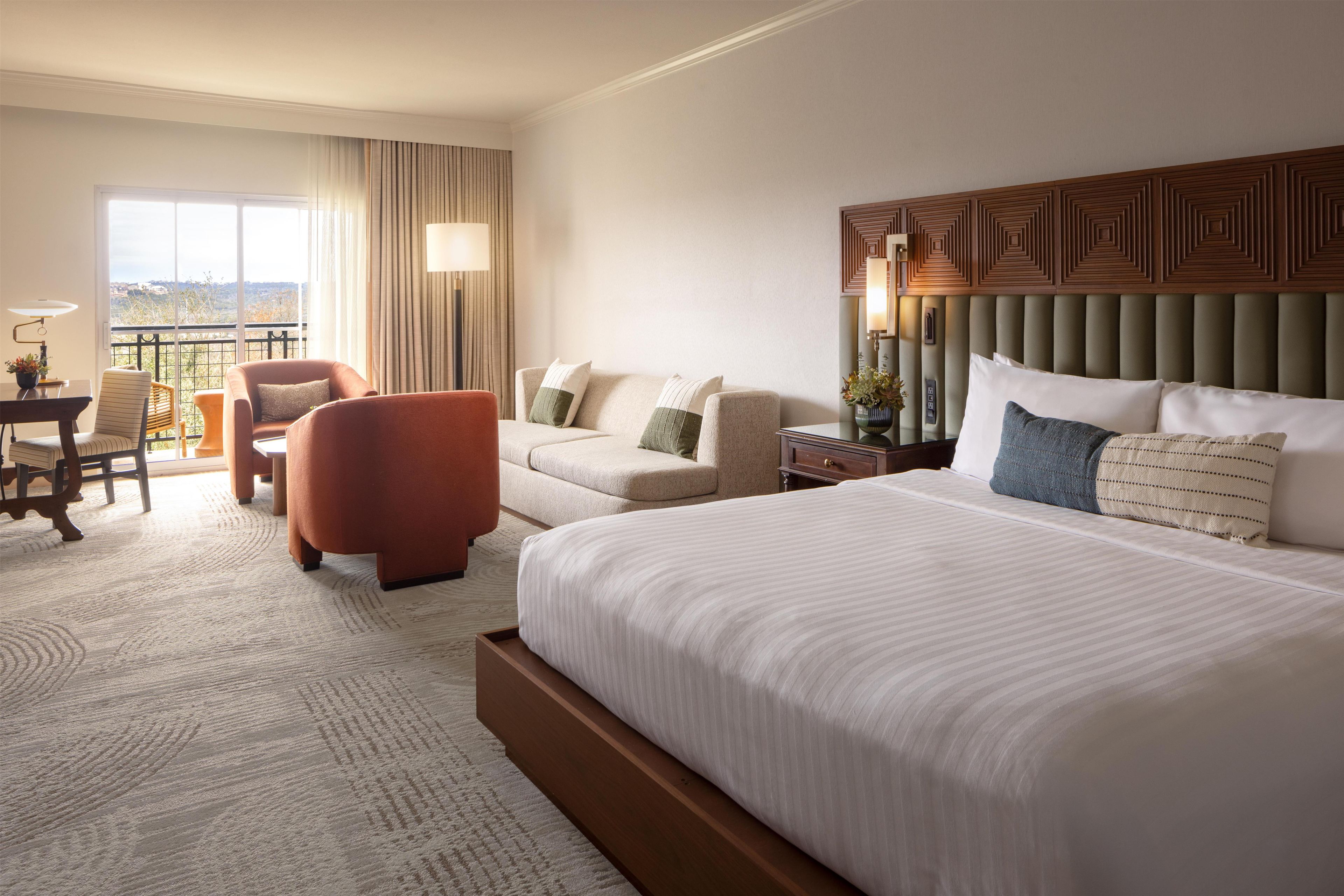 A hotel room with a large bed, a sofa, a chair, a desk, and a view of the outdoors.