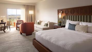 A hotel room with a large bed, a sofa, a chair, a desk, and a view of the outdoors.