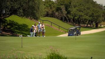 Ein Golfplatz mit einer Gruppe von Personen in der Nähe eines Flaggestangs, einem Golfwagen und einer Treppe, die einen Hügel hinaufführt.