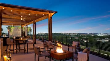 An outdoor patio with a fire pit, seating, and a view of the cityscape at dusk.