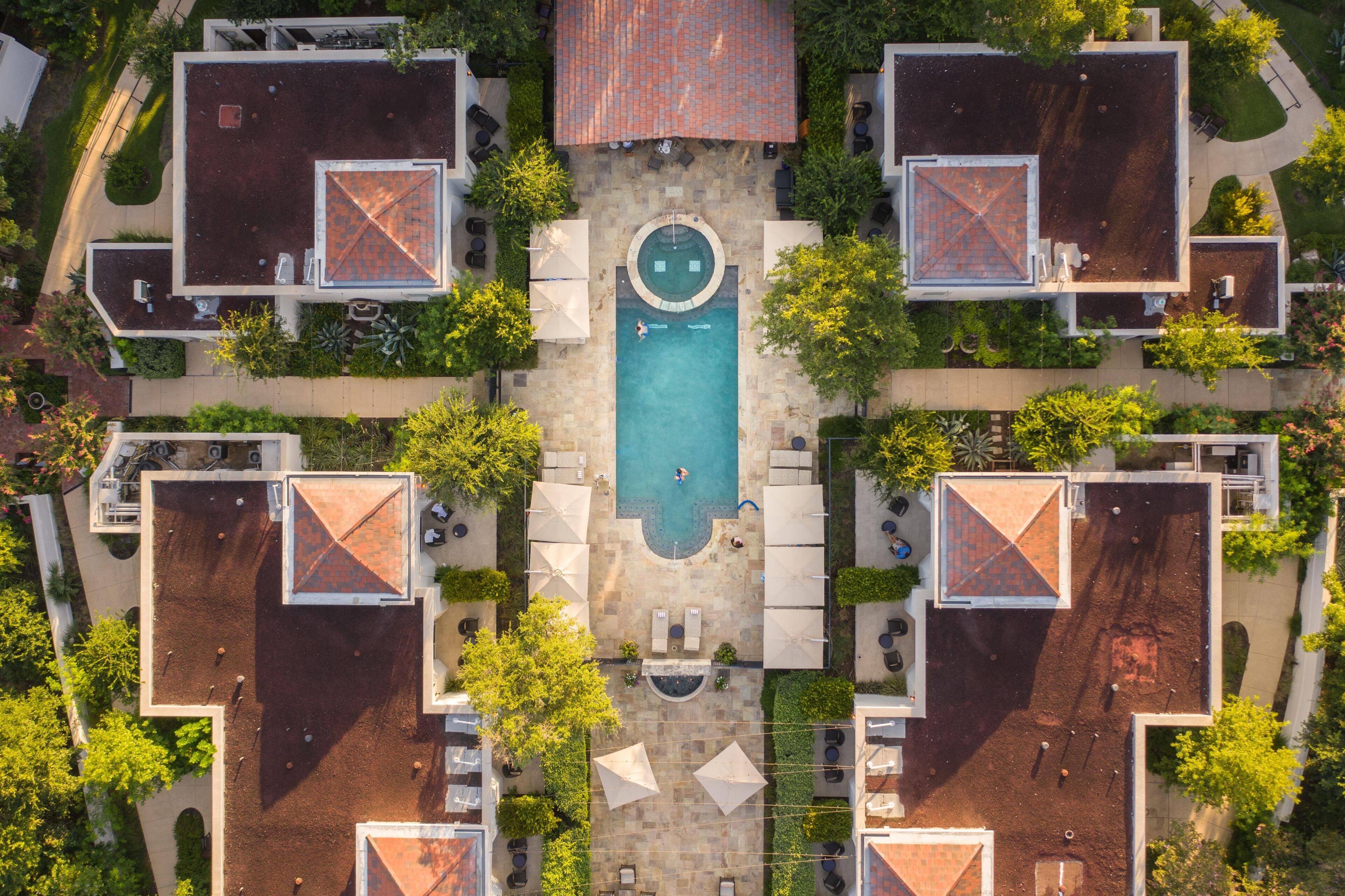 An aerial view of a hotel with a central swimming pool, multiple rooms with red-tiled roofs, and outdoor seating areas.