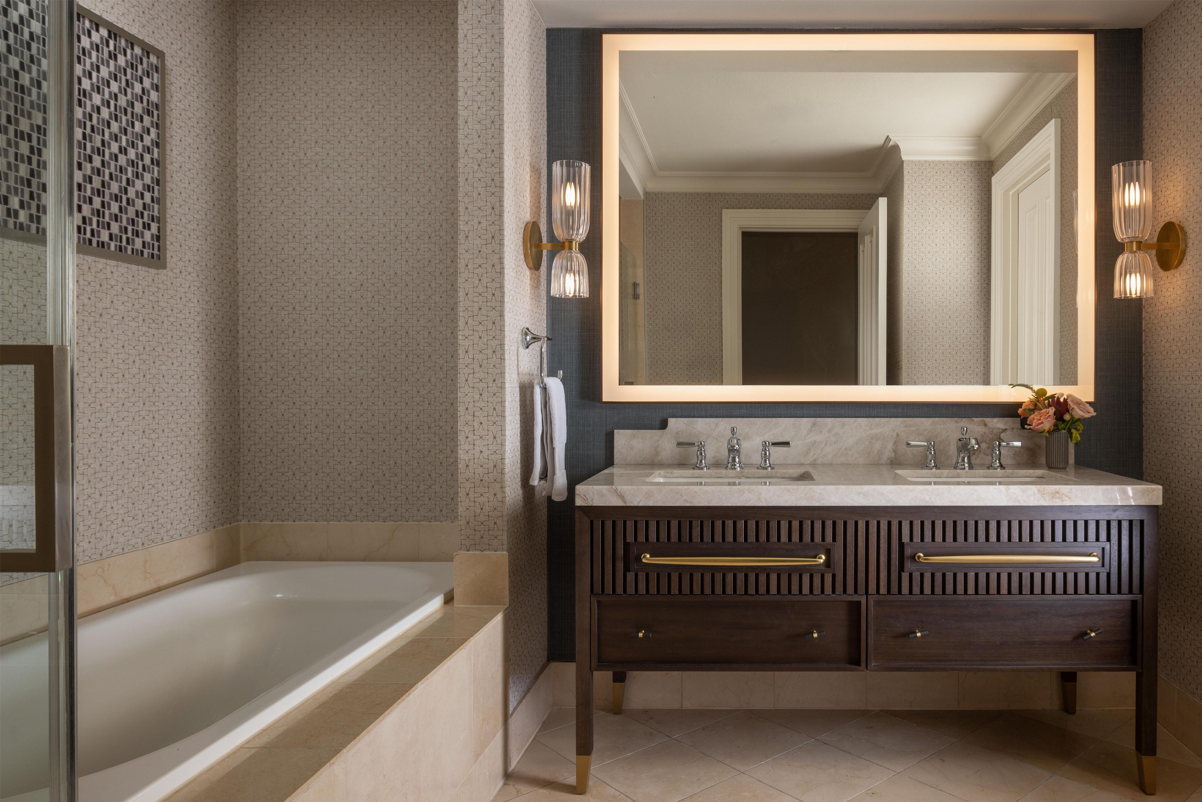 Une salle de bain avec une baignoire, un grand miroir et un meuble-lavabo doté de deux vasques.