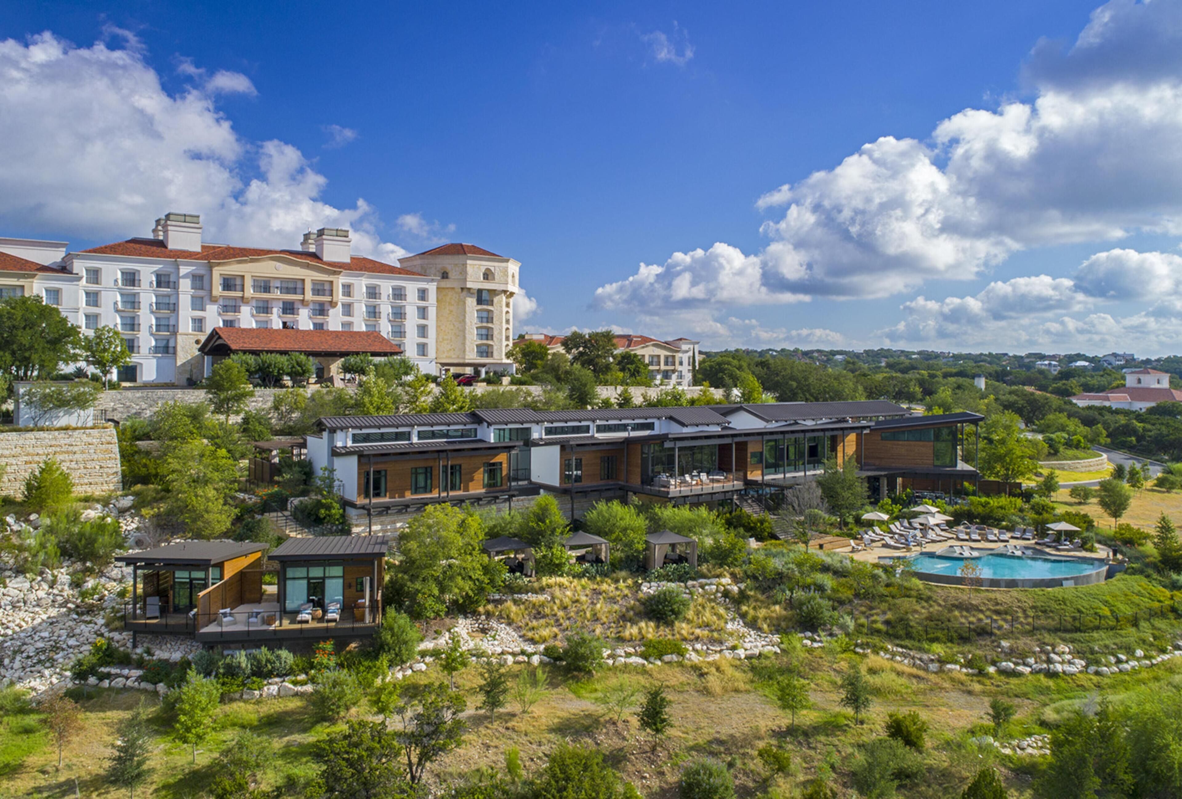 A modern hotel with multiple buildings, a pool, and surrounding greenery.