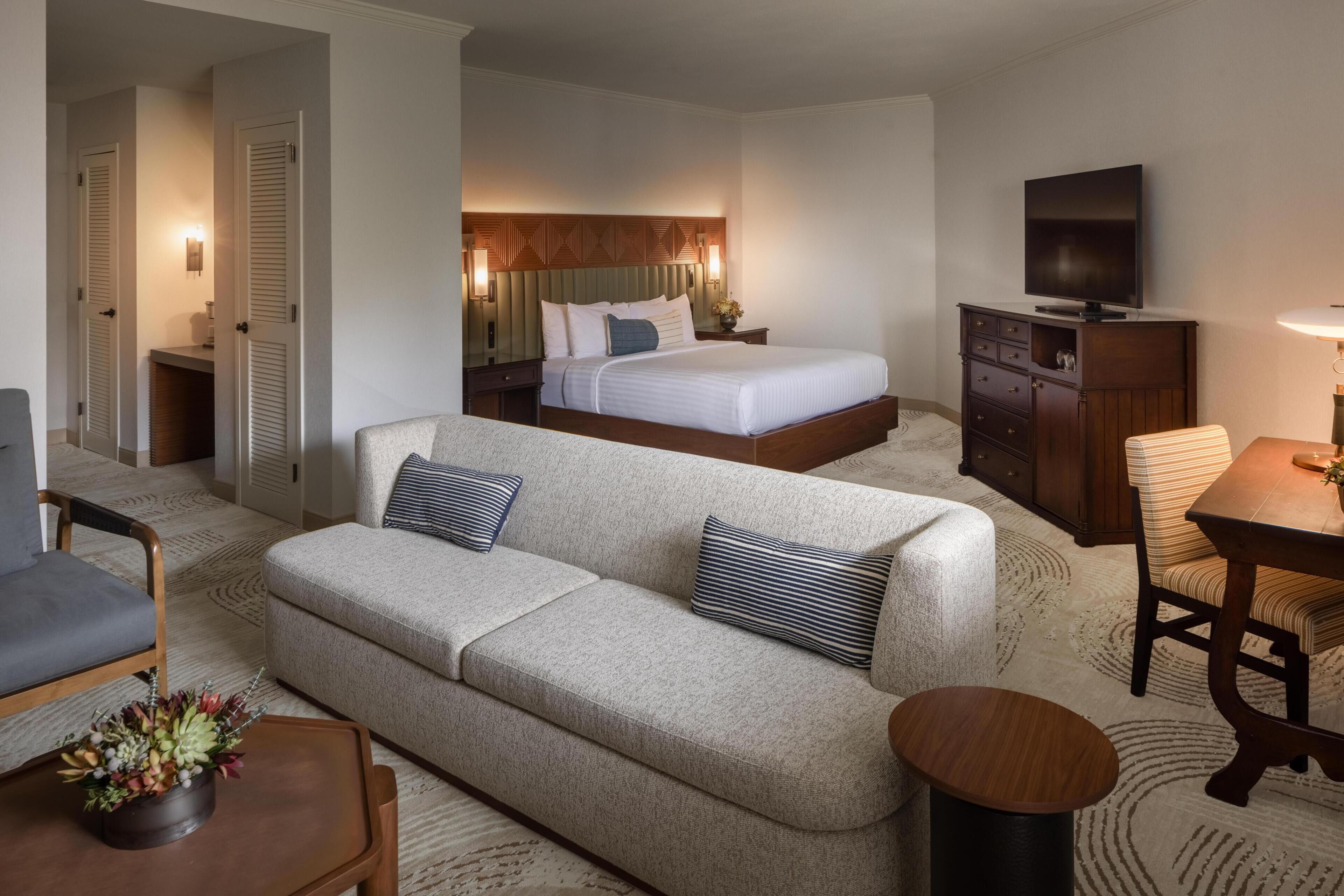 A hotel room with a bed, a sofa, a TV, a desk, and a chair.